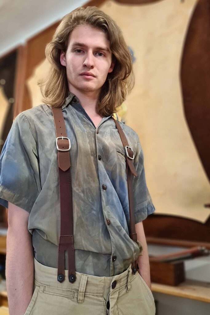Junger Mann mit modisch braunem Lederhosenträger "Hepco Original". Her hosenträger hat zwei robuste Gürtelschnallen.