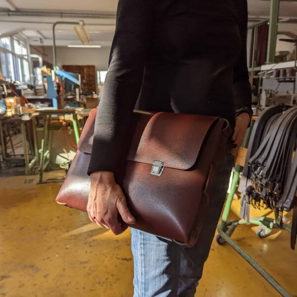 Eine Frau präsentiert die Tasche Blyss von Hepco in der Hepco Manufaktur in der nähe von Stuttgart. Sie hält sie in das Sonnenlicht. Die Tasche ist braun.